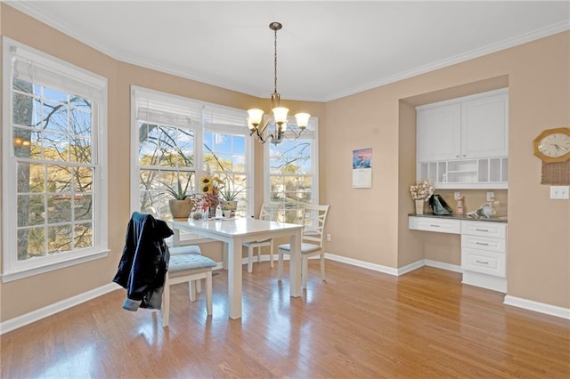 dining area featuring built in desk, ornamental molding, a chandelier, and light wood-type flooring