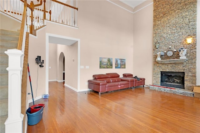 living room featuring hardwood / wood-style flooring, a towering ceiling, ornamental molding, and a fireplace