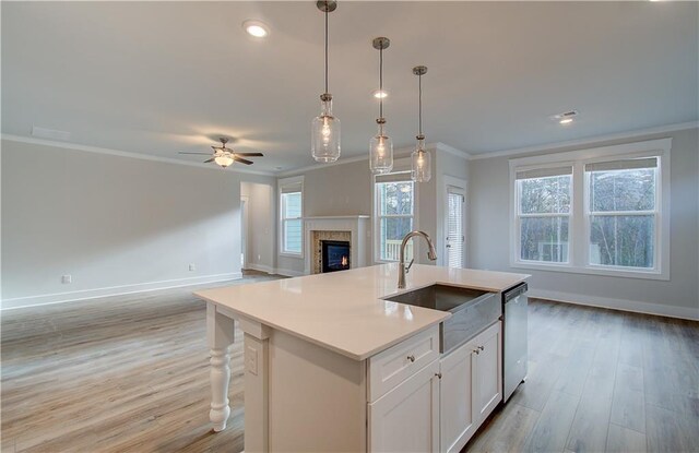 kitchen with ceiling fan, dishwasher, a kitchen island with sink, white cabinets, and ornamental molding