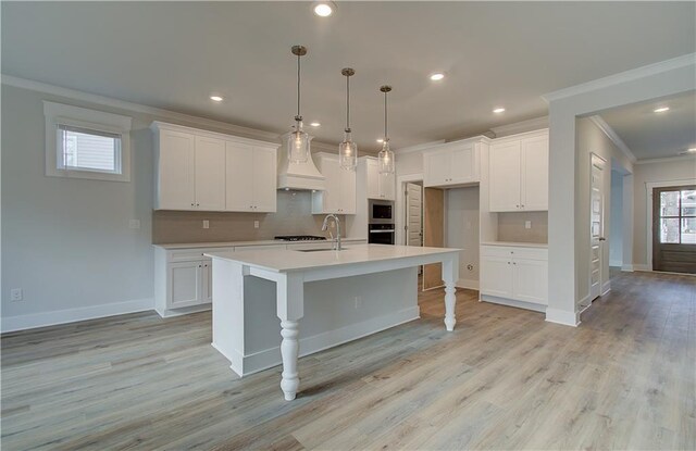 kitchen featuring stainless steel appliances, a center island with sink, white cabinetry, and a wealth of natural light