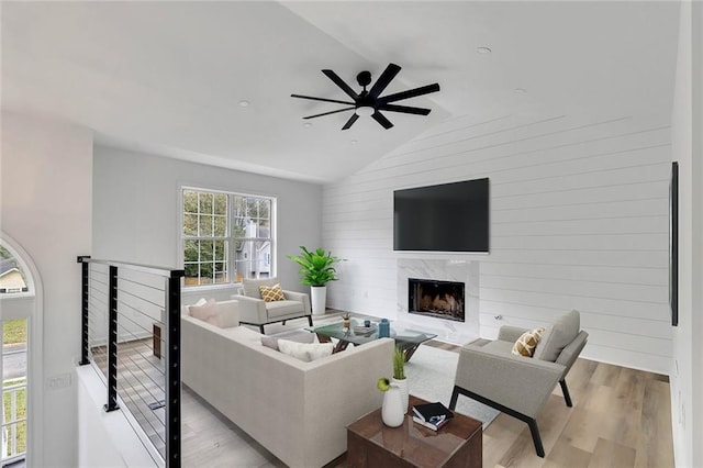 living room with wooden walls, lofted ceiling, ceiling fan, a premium fireplace, and light hardwood / wood-style floors