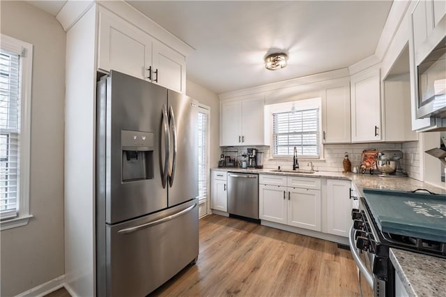 kitchen featuring light wood finished floors, a sink, stainless steel appliances, white cabinets, and backsplash