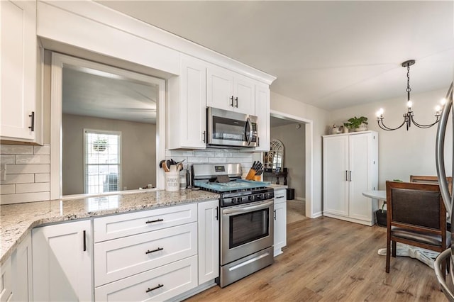 kitchen featuring a chandelier, light stone counters, light wood-style floors, white cabinets, and stainless steel appliances