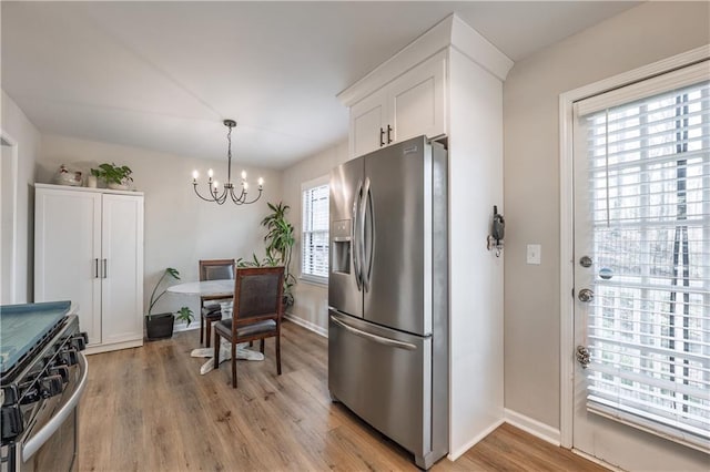 kitchen featuring baseboards, an inviting chandelier, stainless steel appliances, light wood-style floors, and white cabinetry