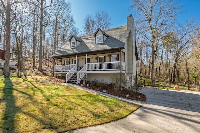 view of front of home with a chimney, aphalt driveway, covered porch, a front yard, and stairs