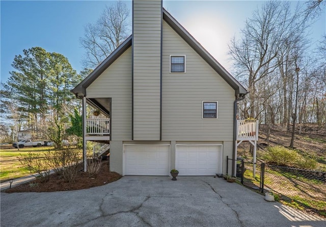 view of property exterior with a garage, fence, a chimney, and aphalt driveway