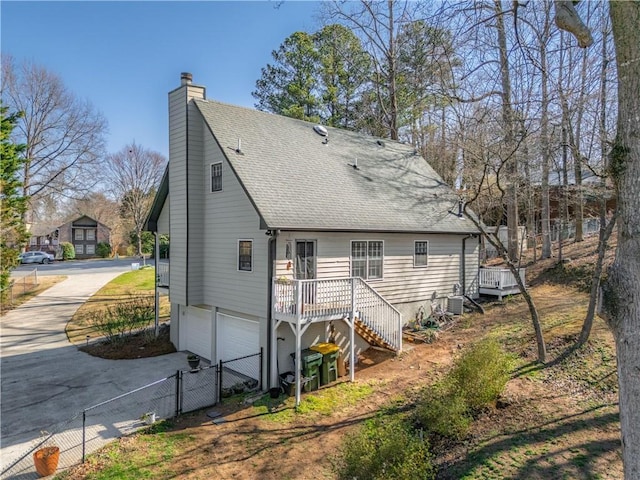 rear view of property with driveway, fence, roof with shingles, a garage, and stairs