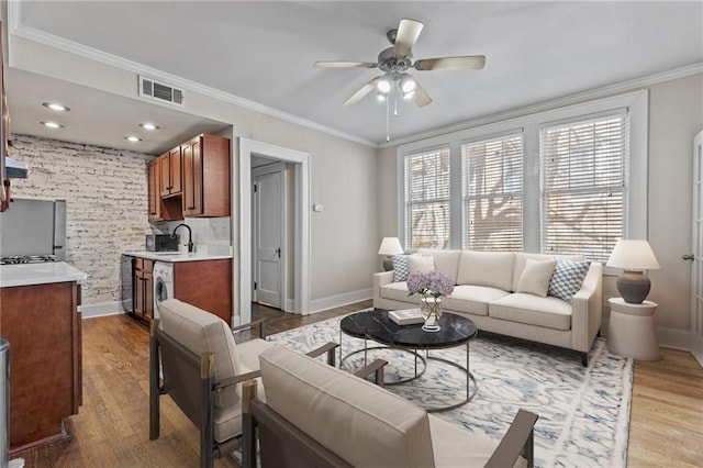 living room with visible vents, baseboards, crown molding, and light wood-style floors