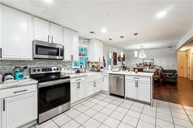 kitchen featuring kitchen peninsula, white cabinetry, stainless steel appliances, pendant lighting, and light hardwood / wood-style flooring