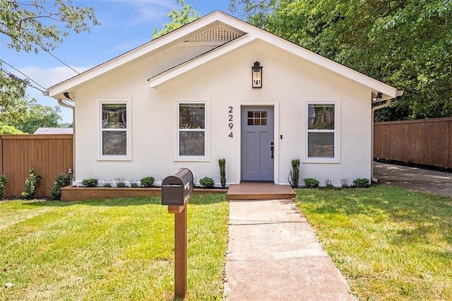 bungalow-style house featuring a front lawn, fence, and stucco siding