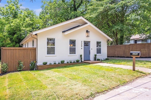 bungalow-style house featuring a front yard, fence, and stucco siding