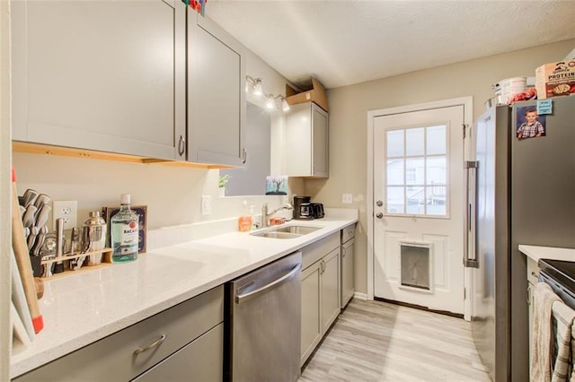 kitchen with light wood-style flooring, gray cabinetry, a sink, light countertops, and appliances with stainless steel finishes