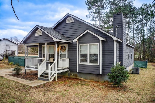 bungalow-style home featuring a shingled roof, a front lawn, central AC unit, covered porch, and a chimney