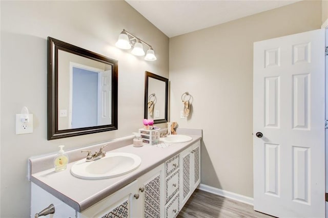 bathroom with double vanity, wood finished floors, baseboards, and a sink