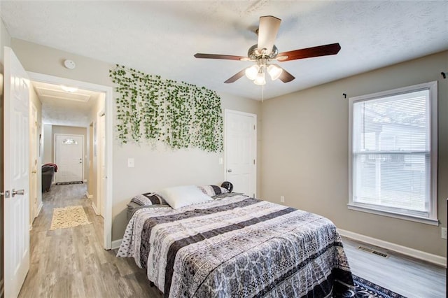 bedroom featuring light wood-type flooring, visible vents, a ceiling fan, a textured ceiling, and baseboards