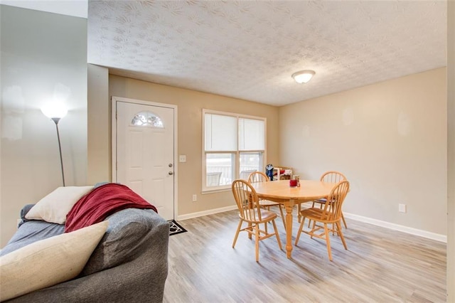 dining room with a textured ceiling, light wood-type flooring, and baseboards