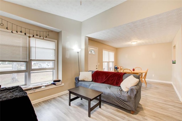 living area featuring light wood-style flooring, a textured ceiling, and baseboards