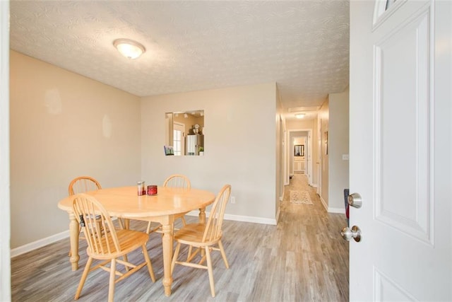 dining area featuring baseboards, light wood finished floors, and a textured ceiling