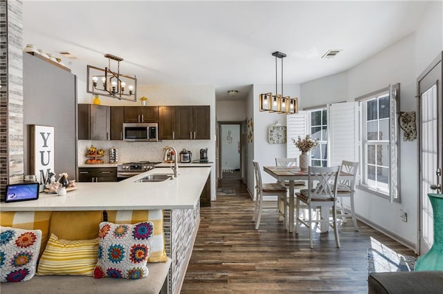 kitchen with tasteful backsplash, stainless steel microwave, dark brown cabinetry, a notable chandelier, and a sink