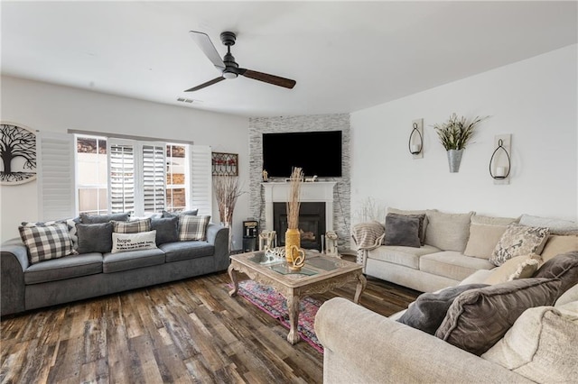 living area with visible vents, a large fireplace, wood finished floors, and a ceiling fan