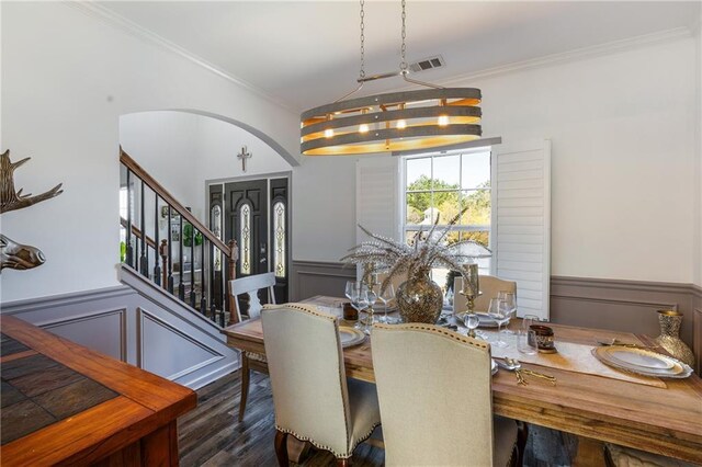 dining space featuring a wainscoted wall, stairway, ornamental molding, wood finished floors, and arched walkways