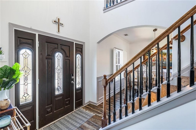 foyer entrance featuring stairway, a healthy amount of sunlight, wood finished floors, arched walkways, and ornamental molding