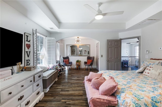 bedroom with a tray ceiling, multiple windows, arched walkways, and dark wood-type flooring