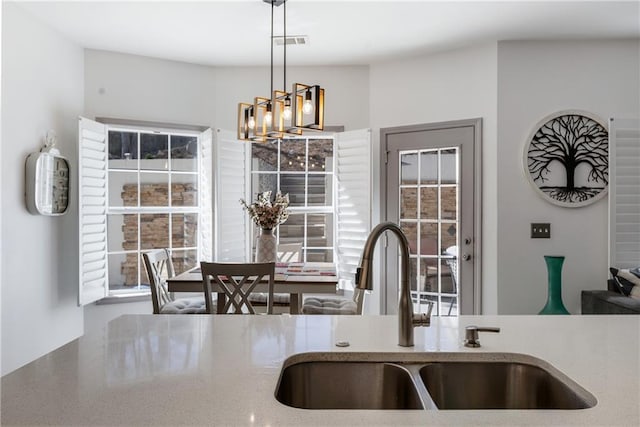 kitchen featuring visible vents, a sink, decorative light fixtures, an inviting chandelier, and light stone countertops
