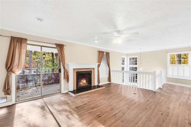 unfurnished living room featuring plenty of natural light, a fireplace, a ceiling fan, and wood finished floors