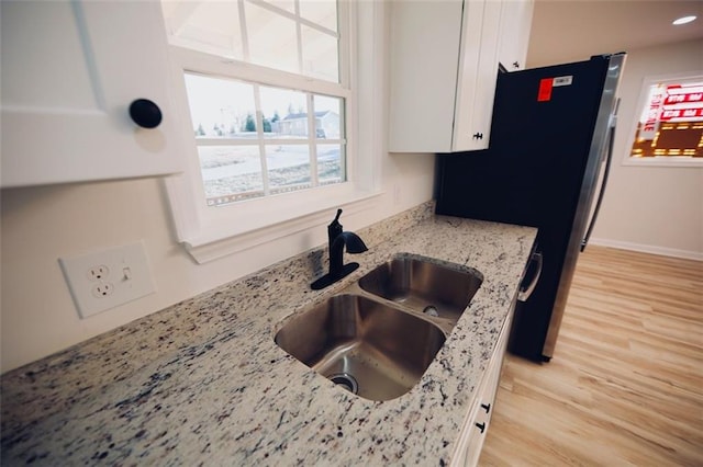 kitchen with light stone countertops, white cabinetry, and sink