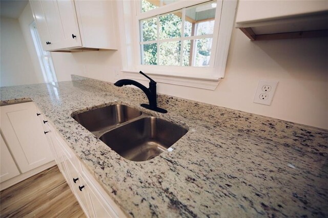 kitchen with white cabinets, light wood-type flooring, light stone counters, and sink