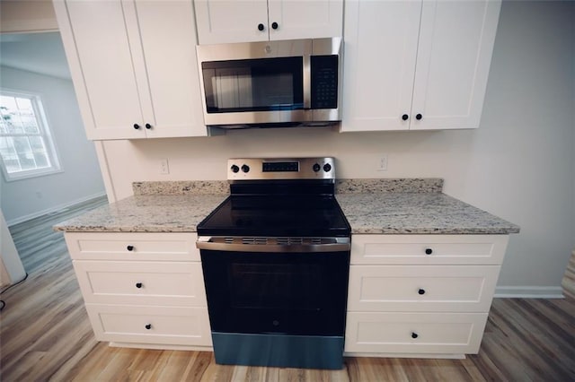 kitchen with white cabinets, light wood-type flooring, stainless steel appliances, and light stone countertops