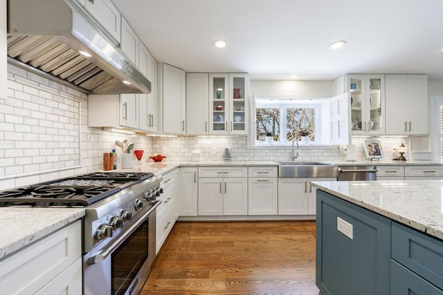 kitchen featuring stainless steel appliances, white cabinets, a sink, light wood-type flooring, and exhaust hood