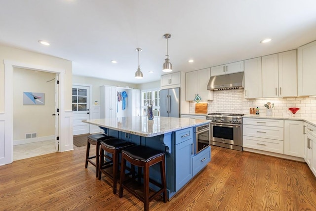 kitchen with light stone counters, under cabinet range hood, stainless steel appliances, visible vents, and dark wood finished floors