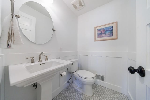 bathroom featuring a wainscoted wall, toilet, visible vents, and a decorative wall