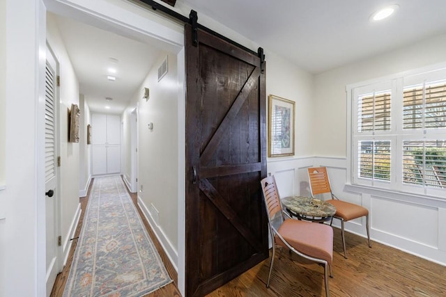 hall with visible vents, a decorative wall, a barn door, wainscoting, and wood finished floors