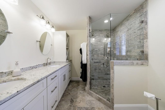 full bathroom featuring double vanity, a shower stall, baseboards, and a sink