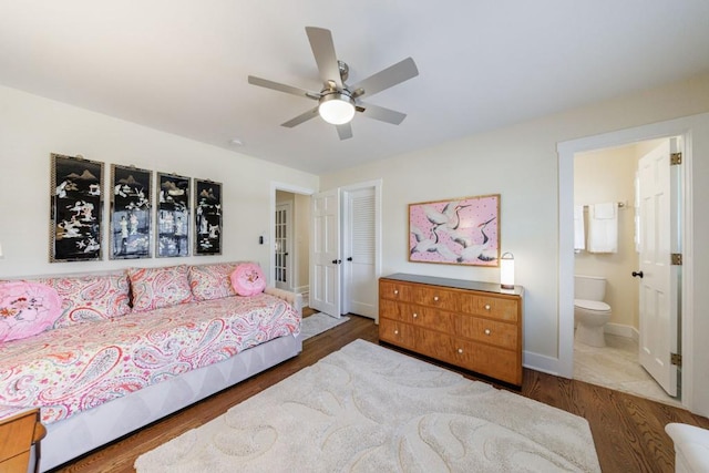 bedroom with baseboards, ceiling fan, ensuite bathroom, and wood finished floors