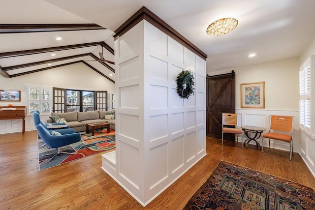 hallway featuring vaulted ceiling with beams, a barn door, a decorative wall, a wainscoted wall, and light wood finished floors