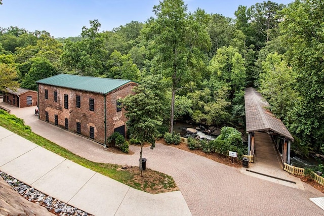 view of side of home featuring decorative driveway, brick siding, metal roof, and a view of trees