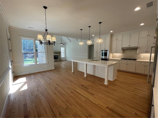 kitchen featuring a kitchen island with sink, pendant lighting, and light wood-type flooring