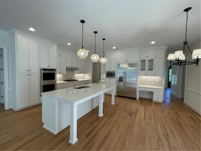 kitchen with built in appliances, sink, white cabinets, light hardwood / wood-style floors, and decorative light fixtures