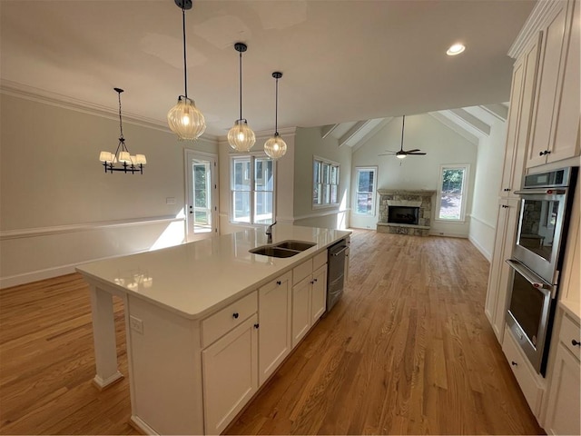 kitchen featuring ceiling fan with notable chandelier, sink, a stone fireplace, light hardwood / wood-style flooring, and a kitchen island with sink