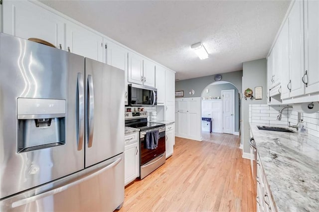 kitchen featuring backsplash, appliances with stainless steel finishes, arched walkways, a sink, and white cabinets