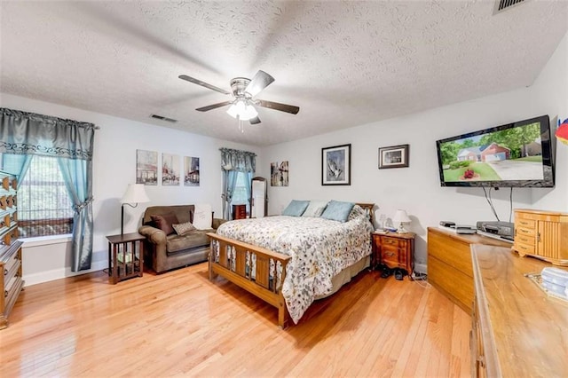 bedroom with baseboards, a textured ceiling, light wood finished floors, and visible vents