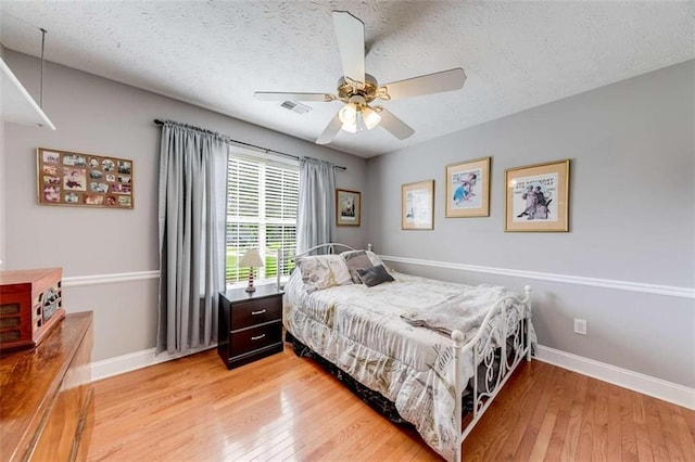 bedroom with light wood-style floors, a textured ceiling, baseboards, and visible vents