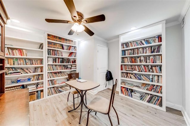 office featuring wall of books, ornamental molding, ceiling fan, and wood finished floors