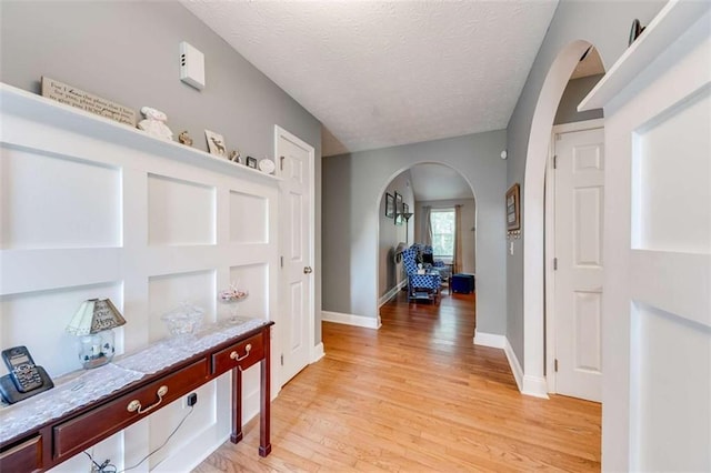 hallway featuring arched walkways, baseboards, a textured ceiling, and light wood-style floors
