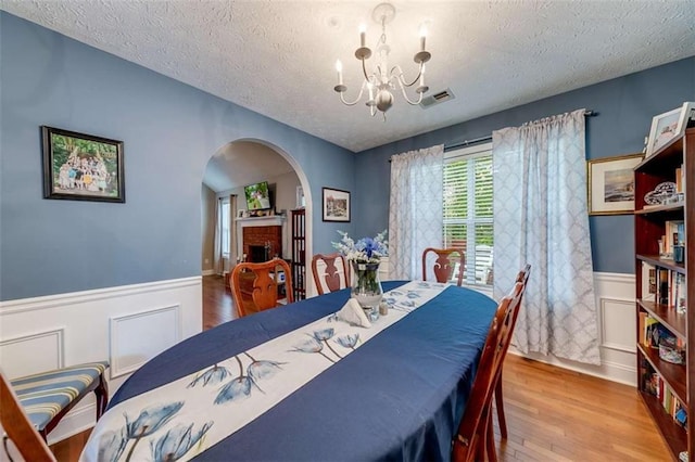 dining area with arched walkways, a textured ceiling, a notable chandelier, and wainscoting