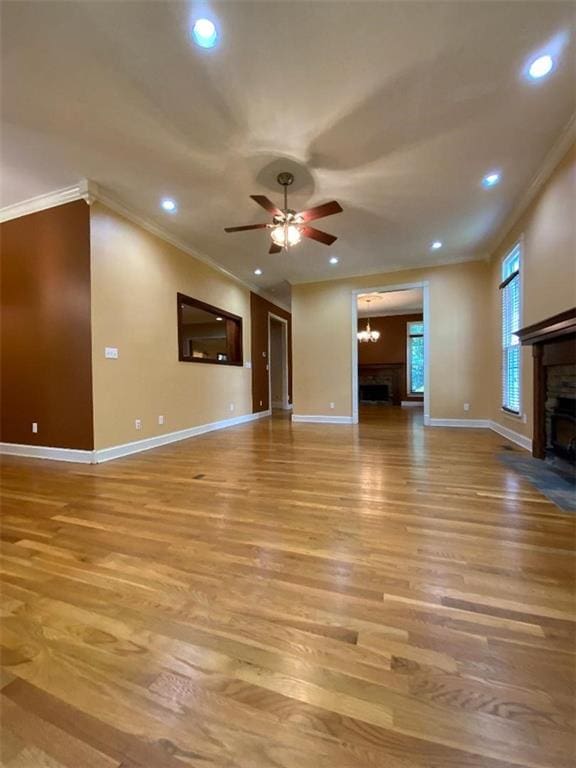 unfurnished living room featuring ceiling fan with notable chandelier, light hardwood / wood-style floors, and crown molding